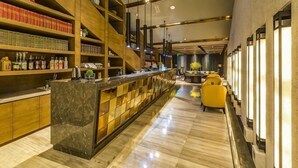 Zona de bar con estantes de botellas, una barra de mármol y un área de estar con sillas amarillas.