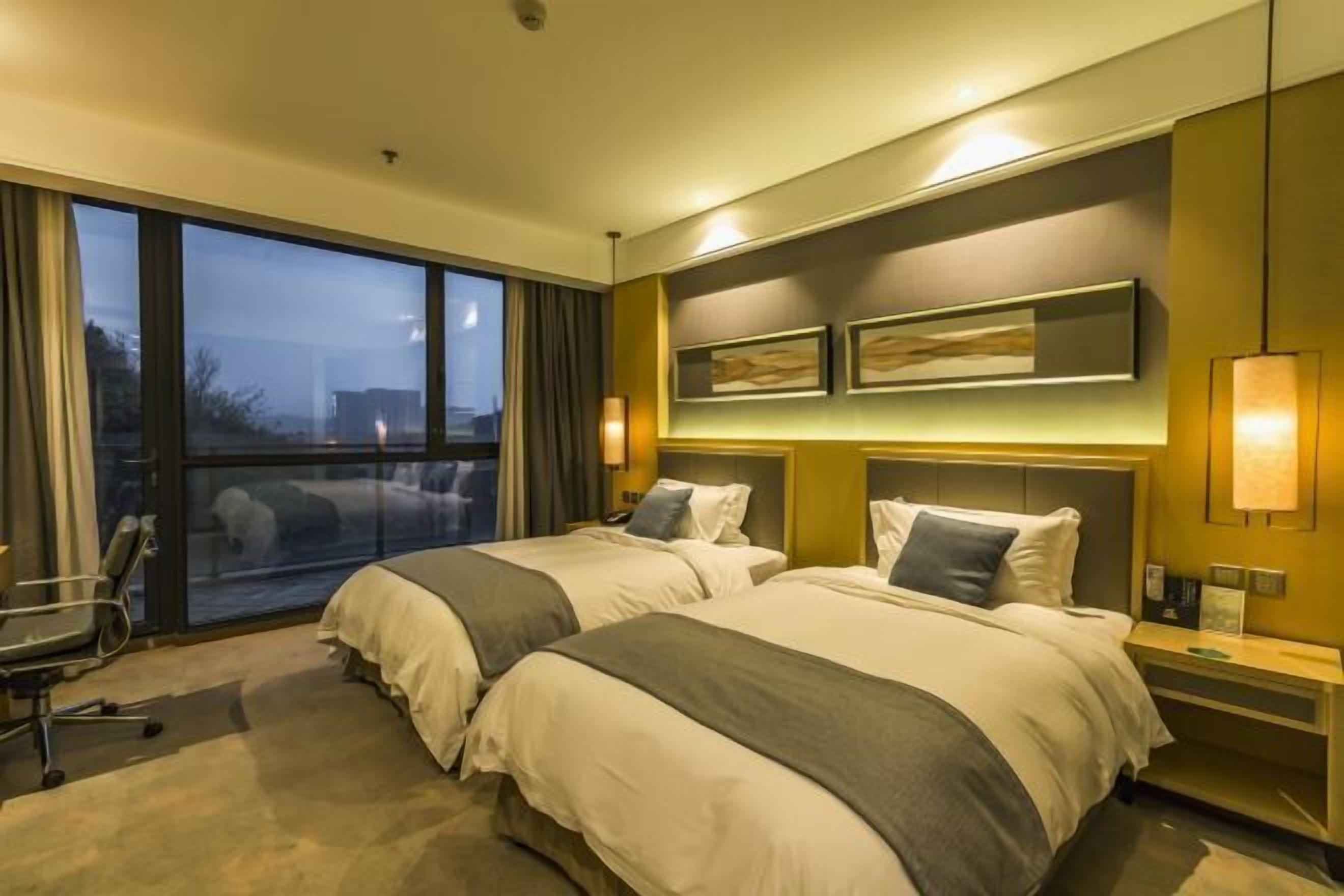 A hotel room with two beds, a large window, a desk, and a chair.