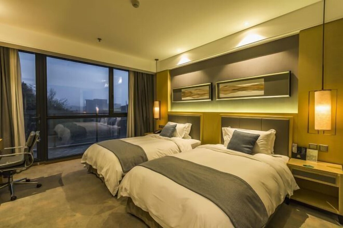 A hotel room with two beds, a large window, a desk, and a chair.