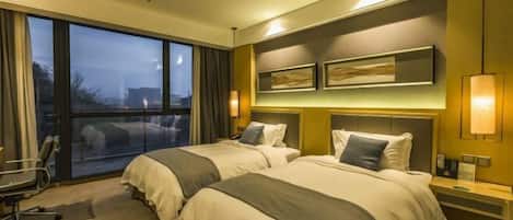 A hotel room with two beds, a large window, a desk, and a chair.