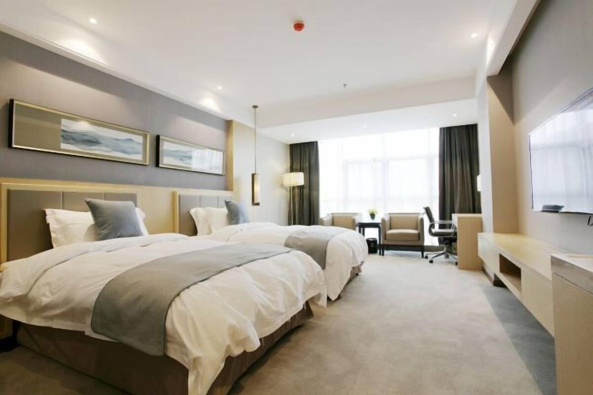 A hotel room with two beds, a desk, a chair, and a TV on the wall.