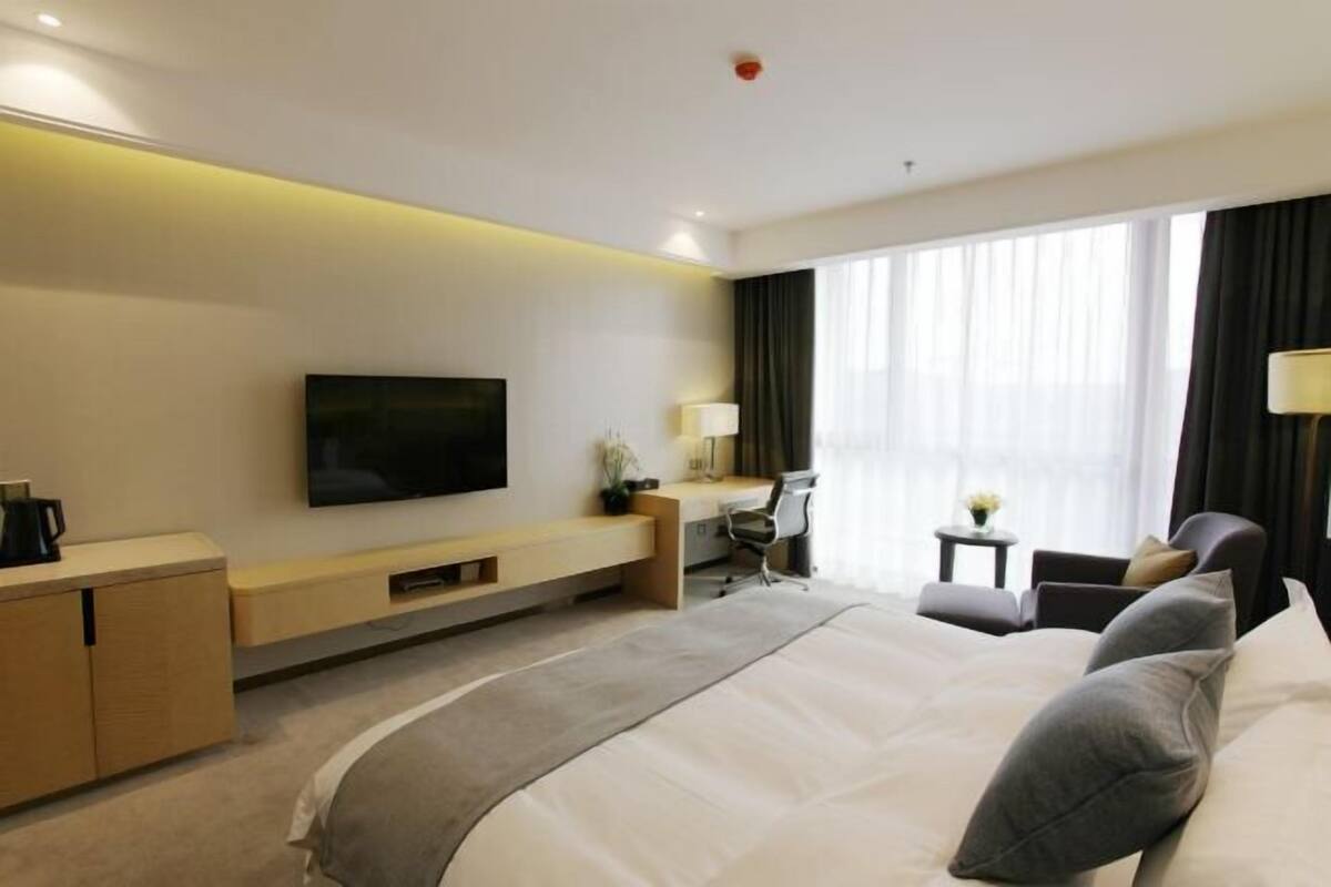 A hotel room with a large bed, a desk, a chair, a TV, and a window with curtains.