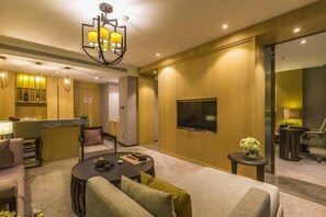 Una habitación de hotel moderna con un sofá, una mesita redonda pequeña, un televisor montado en la pared y una zona de cocina al fondo.