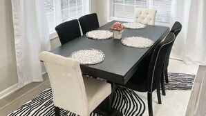 A dining room with a dark wooden table, white chairs, and a zebra-patterned rug.