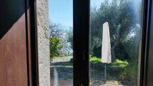 A view through a glass door of an outdoor area with a white umbrella, stone wall, and greenery. - A True Sicilian guesthouse with Pool on Mt. Etna, perfect for Families & Groups. (Puntalazzo)