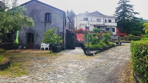 A cobblestone street leading to a building with a stone facade and a red door. - A True Sicilian guesthouse with Pool on Mt. Etna, perfect for Families & Groups. (Puntalazzo)