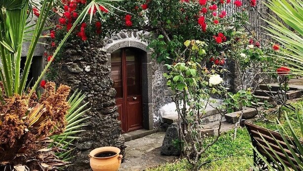 A stone building with a wooden door, surrounded by lush greenery and red flowers. - A True Sicilian guesthouse with Pool on Mt. Etna, perfect for Families & Groups. (Puntalazzo)