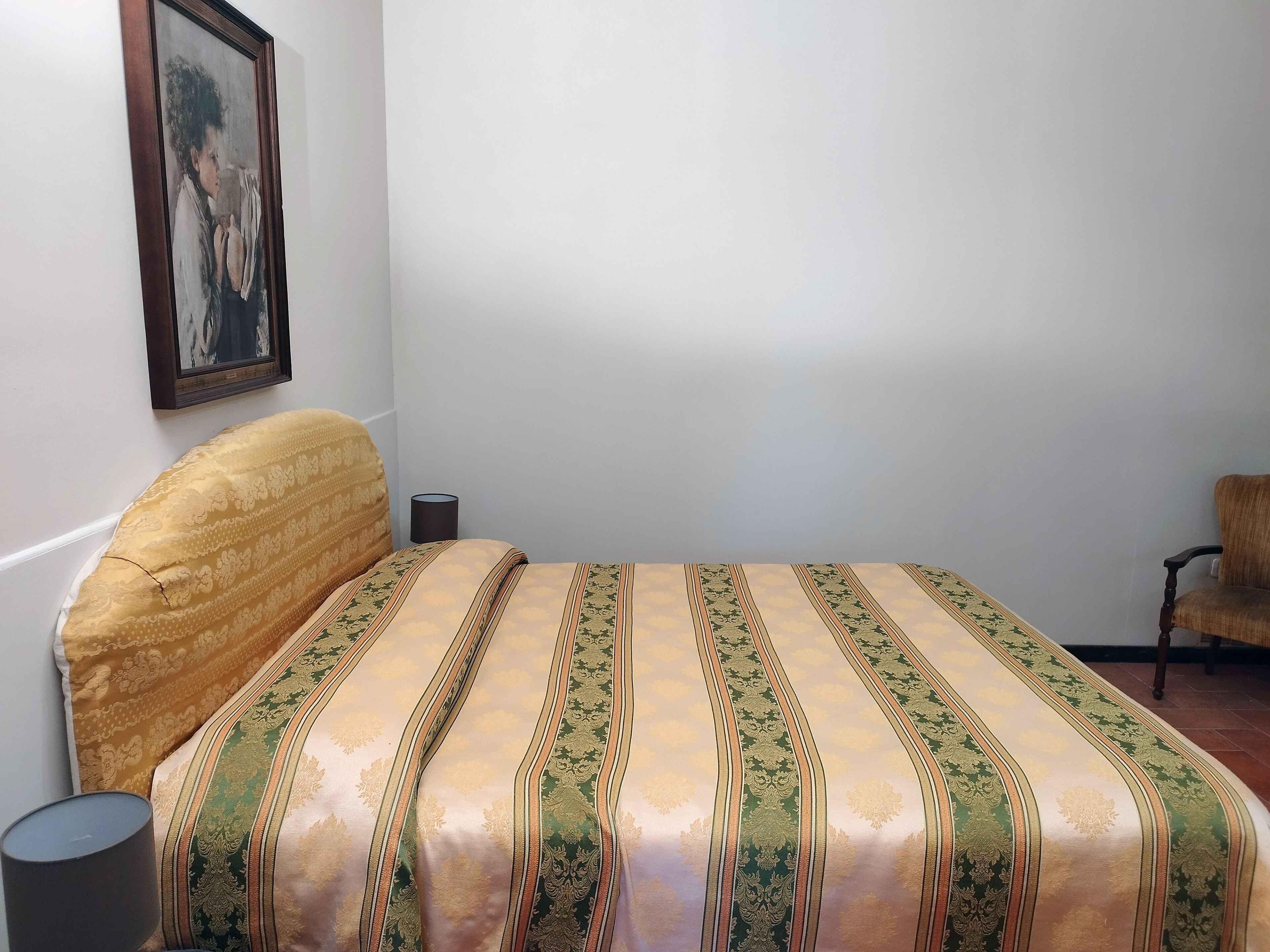 Une chambre à coucher avec un lit, une chaise, une lampe et un tableau encadré accroché au mur.