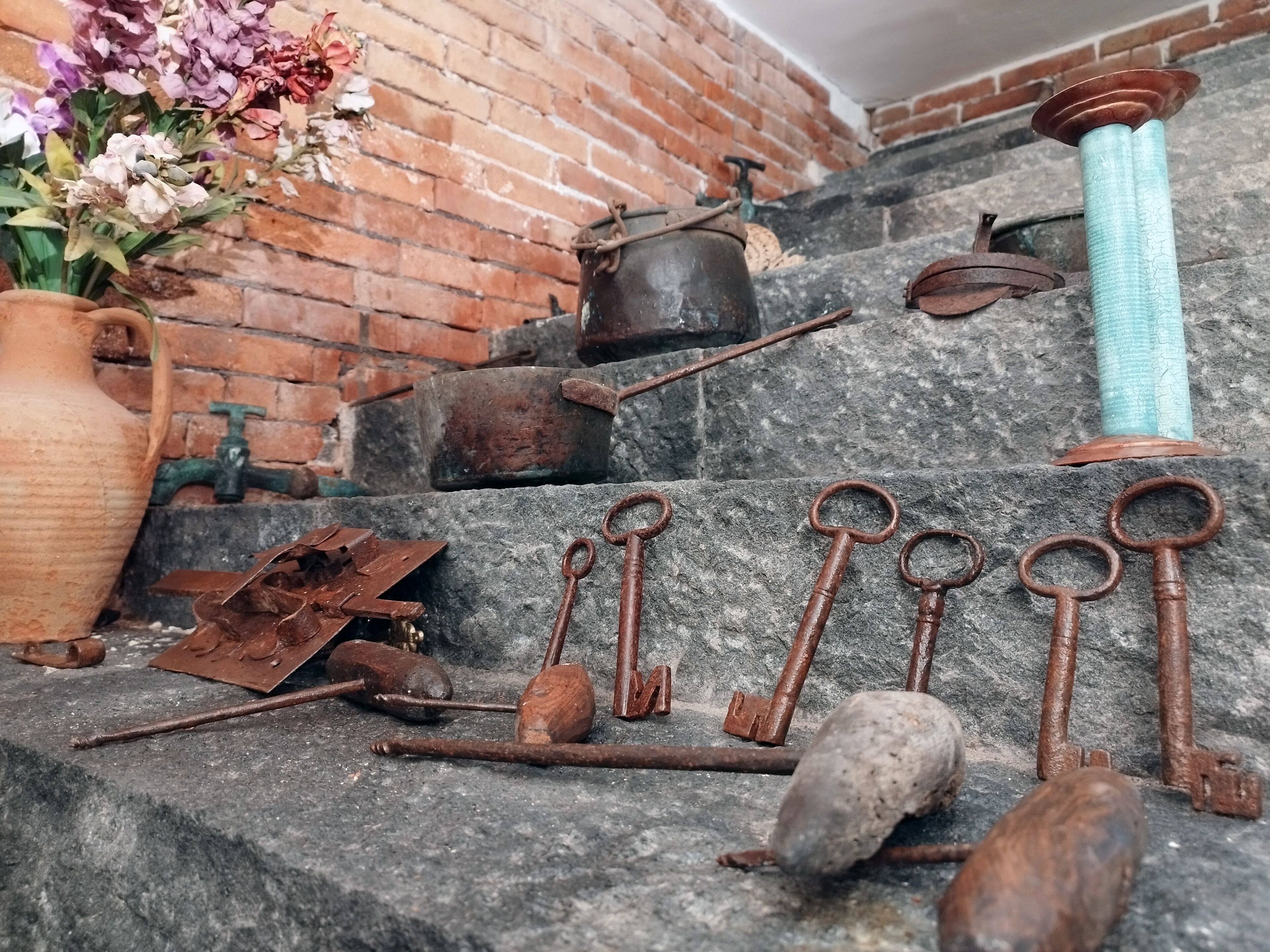 A collection of antique tools and a vase of flowers on stone steps.