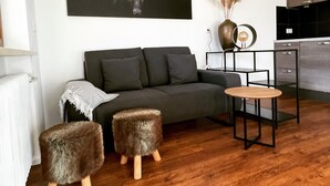 A modern living room with a dark grey sofa, two furry ottomans, a round wooden table, and a black and white artwork on the wall. - Family-friendly temporary home (Horben)