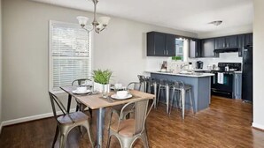 Una cocina moderna con armarios oscuros, una isla central y un comedor con sillas de metal y una mesa de madera.