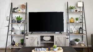 Un salón con una televisión de pantalla plana, armarios de madera y dos estanterías metálicas decoradas.
