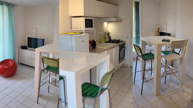 A compact kitchen with white cabinets, a microwave, and a gas stove. There are two dining tables with chairs, and a red bean bag chair is visible.
