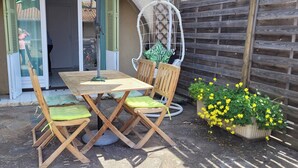 An outdoor patio with a wooden table and chairs, a hanging chair, and potted plants.