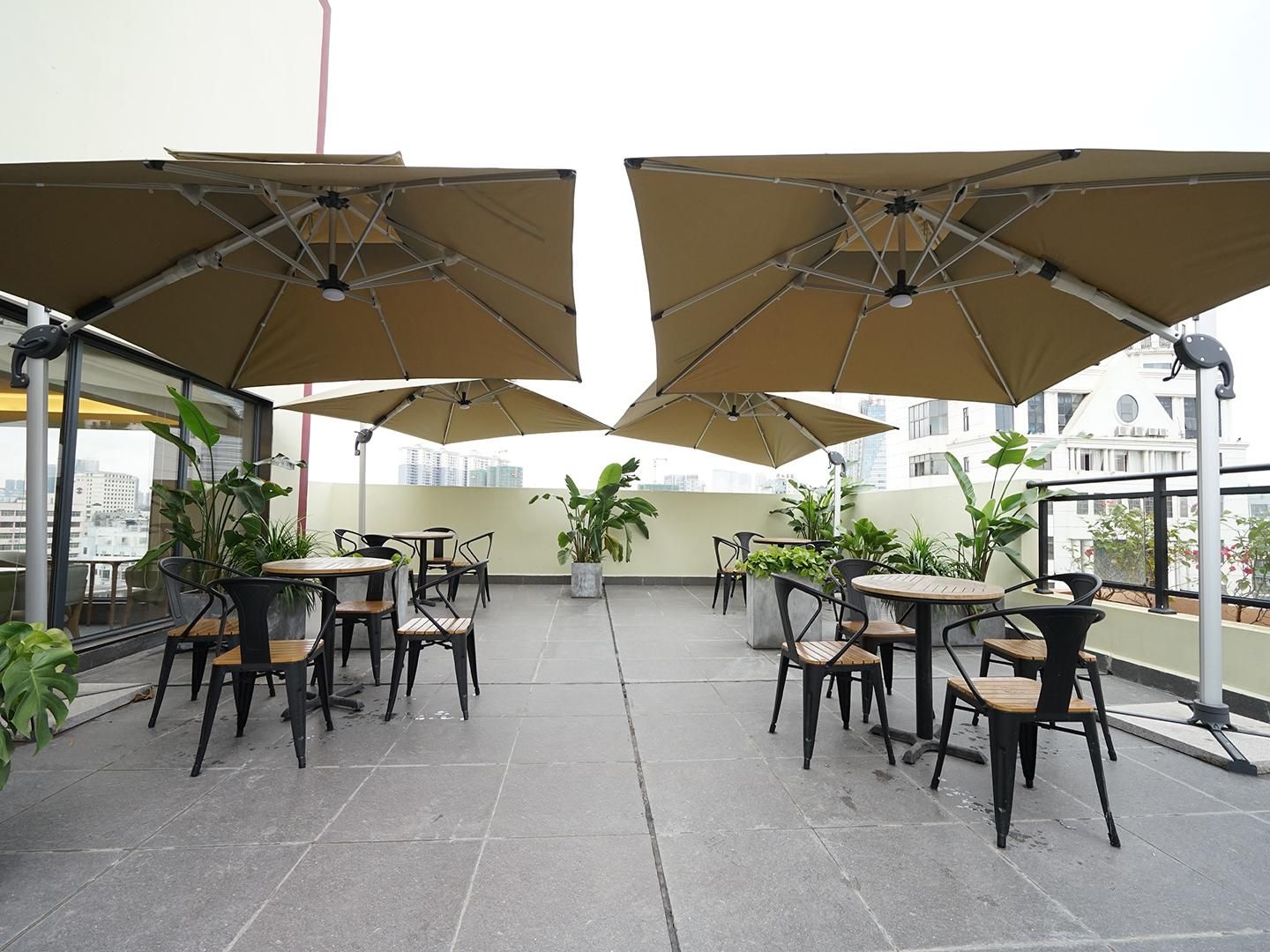 A rooftop terrace with outdoor seating, including tables and chairs, and large umbrellas providing shade.