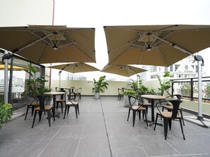 Una terraza en la azotea con mobiliario exterior, incluyendo mesas y sillas, y grandes sombrillas que ofrecen sombra.