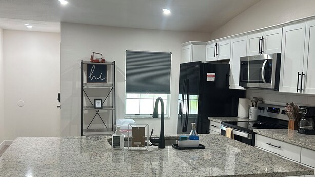 A modern kitchen with a large island, bar stools, a microwave, and a refrigerator.