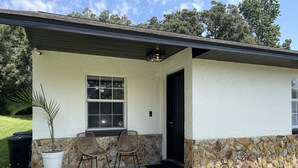 A house with a stone exterior, a porch with two wicker chairs, a potted plant, and a window.