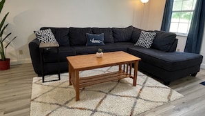 A modern living room with a sectional sofa, a wooden coffee table, and a patterned rug.