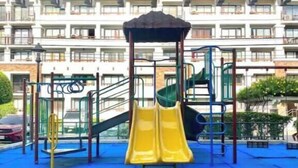 A playground with a yellow slide and climbing structures, set against a backdrop of a multi-story building with balconies. - Convenient 1BR Beside SM Mall (Davao City)