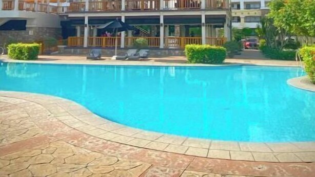 A hotel with a swimming pool, a covered area with seating, and a view of the surrounding landscape. - Convenient 1BR Beside SM Mall (Davao City)