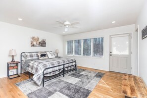 Une chambre à coucher comprenant un lit, une table de chevet, un ventilateur de plafond, une fenêtre avec des stores et une porte.