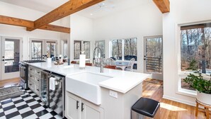 Een ruime keuken met een groot eiland, houten balken en grote ramen met uitzicht op de omgeving.
