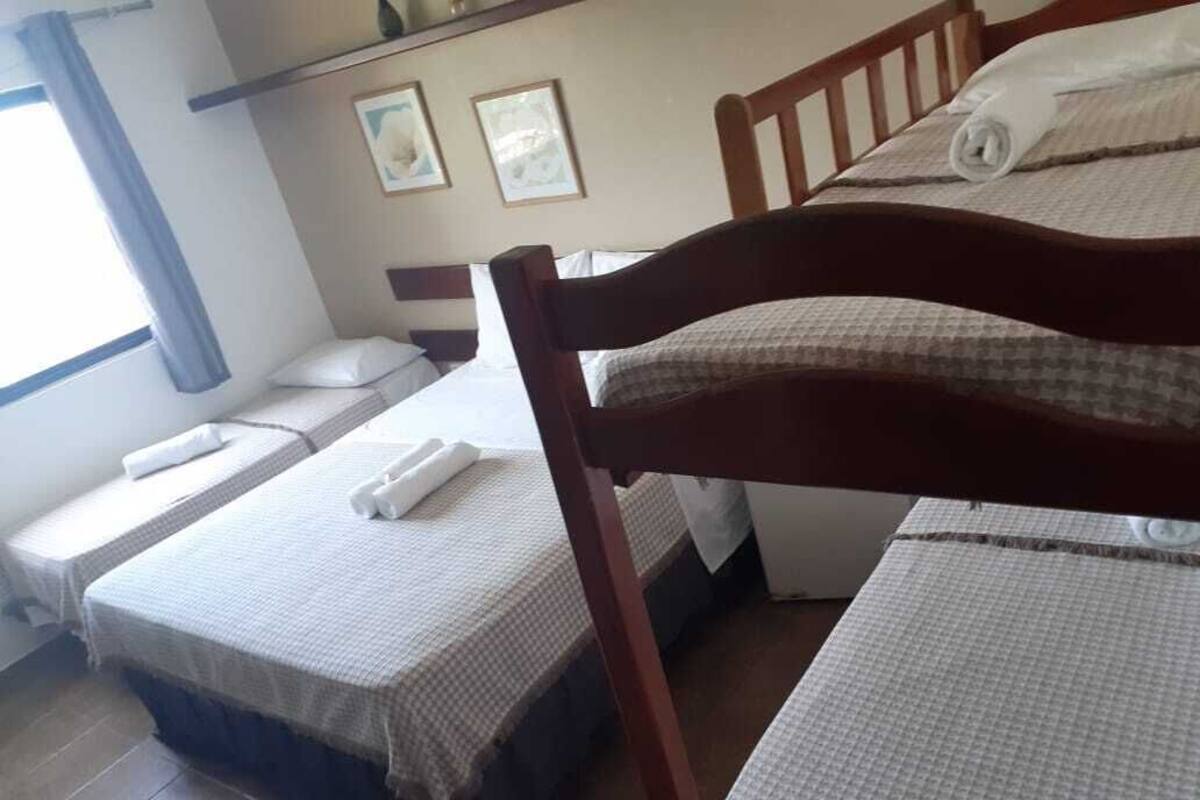Quarto com duas camas de solteiro, cada uma com cabeceira de madeira, roupa de cama branca e uma toalha enrolada. Há duas imagens emolduradas na parede acima das camas.