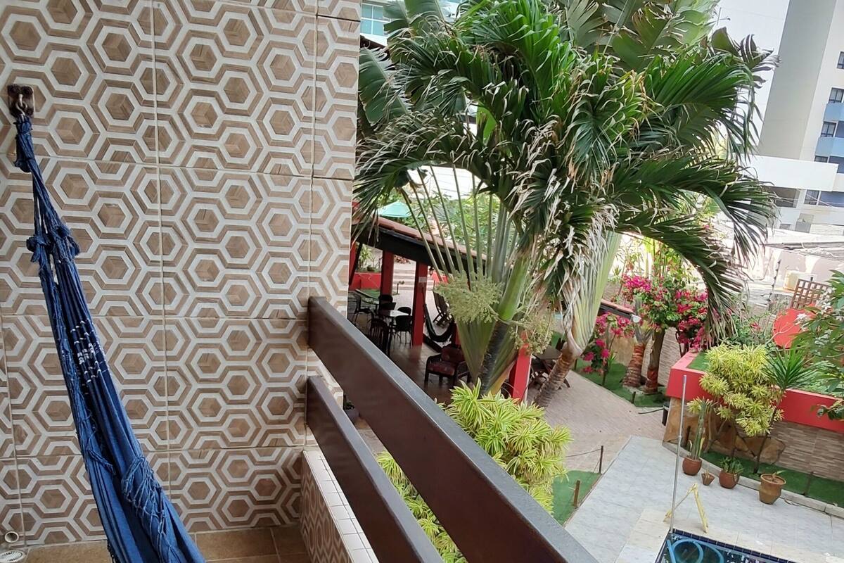 Uma rede em uma varanda com paredes estampadas e vista para um edifício e vegetação.