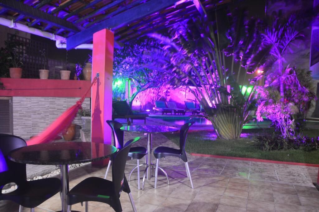 An outdoor patio area with a glass table and chairs, surrounded by potted plants and palm trees.