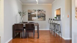 A dining area with a wooden table and chairs, a vase with branches, and a large abstract painting on the wall.