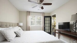 A bedroom with a bed, ceiling fan, TV, and a door leading outside.