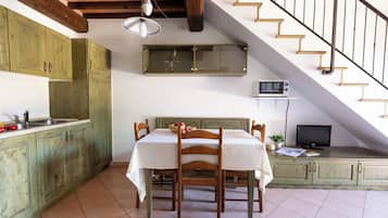 Una cocina con armarios de madera, una mesa de comedor con sillas, un microondas y un televisor sobre una estantería.