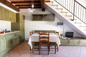 A kitchen with wooden cabinets, a dining table with chairs, a microwave, and a television on a shelf. - Residence Borgo Verde (Rosignano Marittimo)