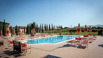 Una piscina con sillas de descanso y sombrillas, rodeada de árboles y un cielo despejado.