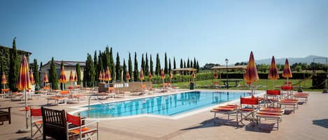 A swimming pool with lounge chairs and umbrellas, surrounded by trees and a clear sky.