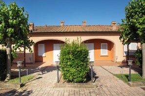 Un bâtiment doté d’un toit en tuiles, de deux portes cintrées et d’un arbuste vert au centre.
