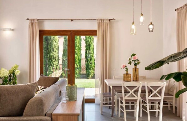 Una sala de estar moderna con un sofá, una mesa de comedor con sillas y vistas a espacios verdes.
