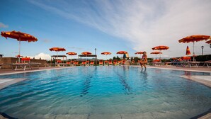 A swimming pool with multiple sun loungers and umbrellas, surrounded by a stone wall and a clear sky. - Residence Borgo Verde (Rosignano Marittimo)