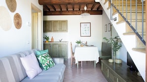 A cozy living room with a sofa, a dining table, and a staircase leading to an upper level. - Residence Borgo Verde (Rosignano Marittimo)