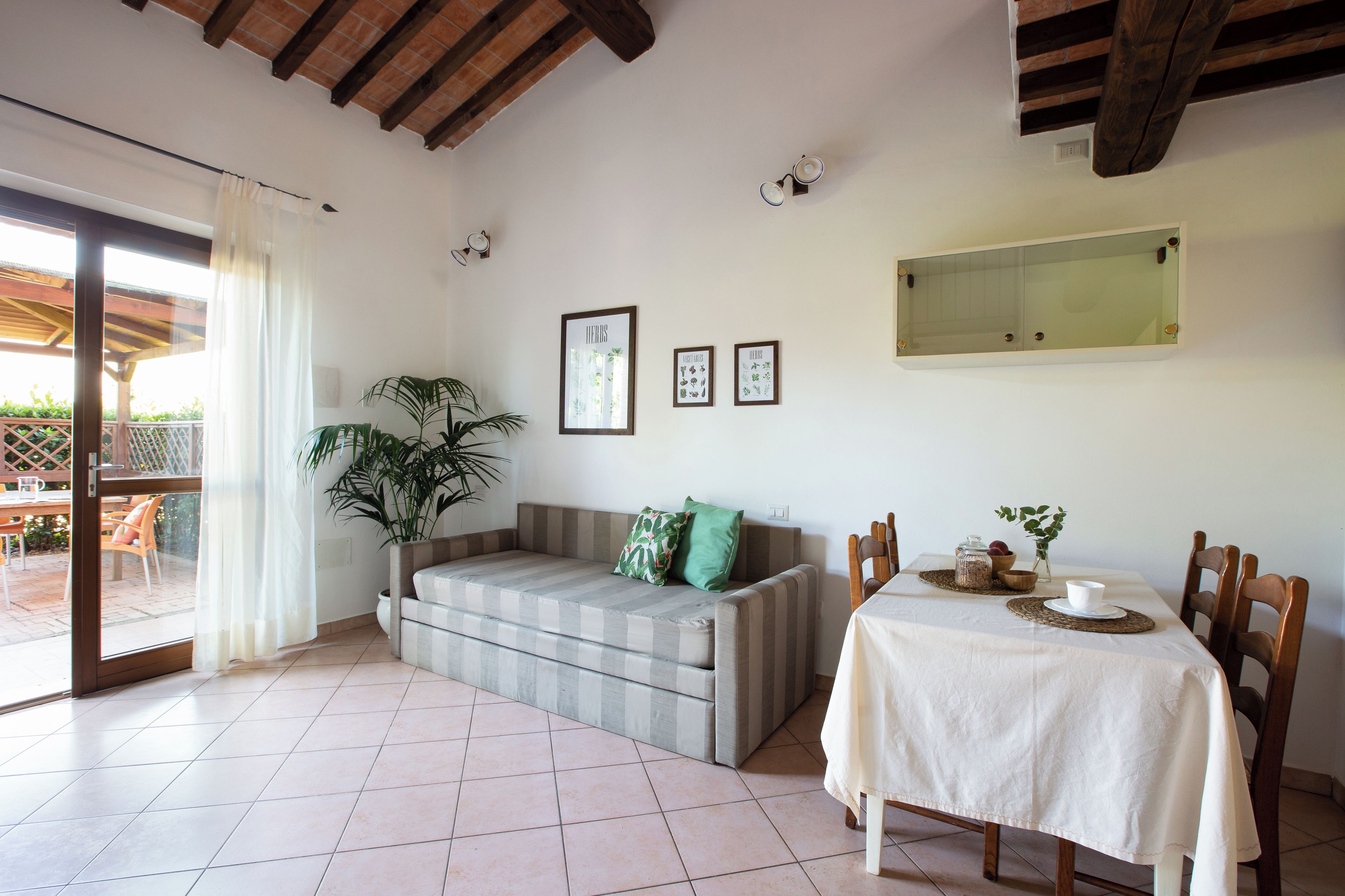 Uma área de jantar com uma mesa posta para dois, um sofá e um vaso com planta.