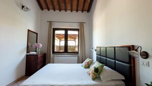 A bedroom with a large bed, a dresser, a mirror, and a window with curtains. - Residence Borgo Verde (Rosignano Marittimo)
