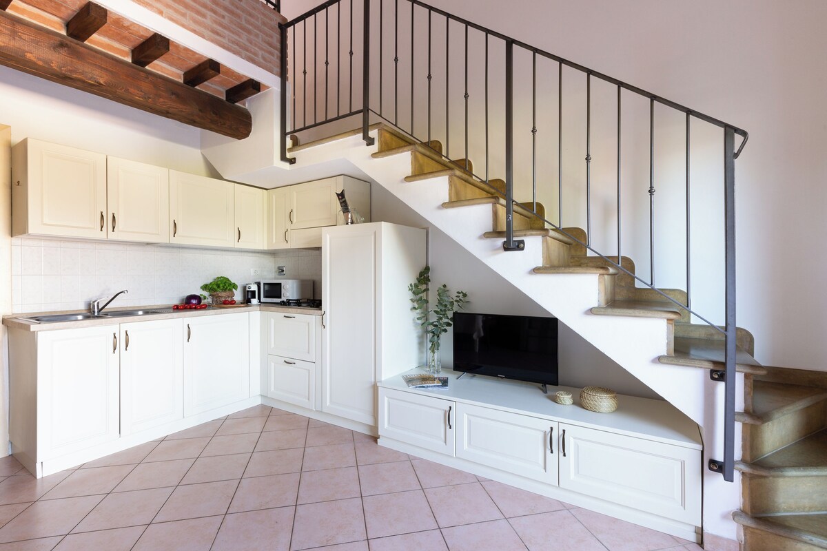 A kitchen with white cabinets, a microwave, and a wooden staircase with a black railing.