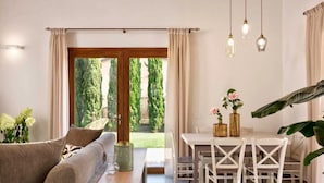 A modern living room with a sofa, a dining table with chairs, and a view of greenery outside. - Residence Borgo Verde (Rosignano Marittimo)