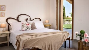 A bedroom with a bed, bedside lamps, a wooden headboard, a window with a view of greenery, and a door leading outside. - Residence Borgo Verde (Rosignano Marittimo)