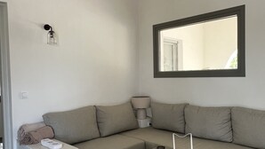 A modern living room with a beige sofa, a small white side table, a wooden coffee table, and a window with a view of the outdoors. - Countryside farm family house, private, calm with mountain views (Sangri)