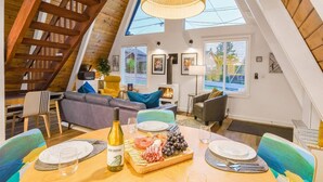 Ein gemütliches Wohnzimmer im Loft-Stil mit Essbereich, ausgestattet mit Kamin, Holzbalken und großen Fenstern.