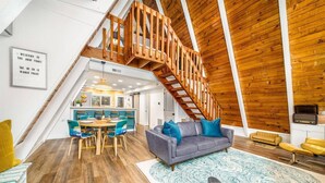 Ein geräumiges Loft mit einer Holztreppe, einem Essbereich und einem Wohnzimmer mit großem Teppich und einer Couch.