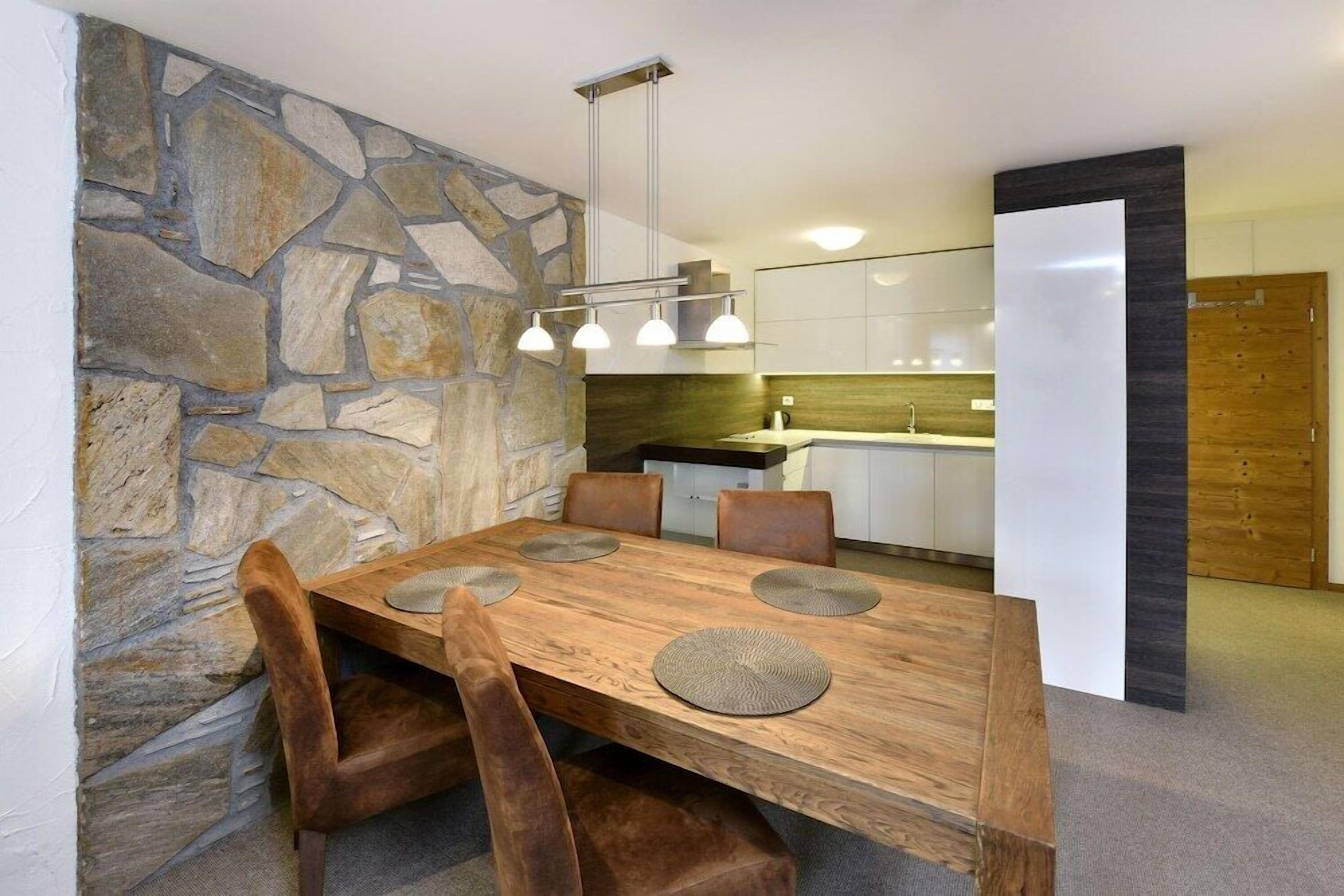 Ein moderner Essbereich mit einer Wand aus Stein, einem Holztisch mit vier Stühlen und einer Pendelleuchte.
