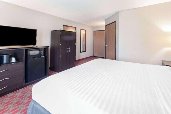 Een hotelkamer met een bed, een flatscreen televisie, een minibar, een kledingkast en een spiegel.